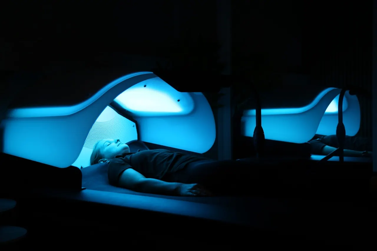Person lying in a blue-lit treatment pod in a darkened room