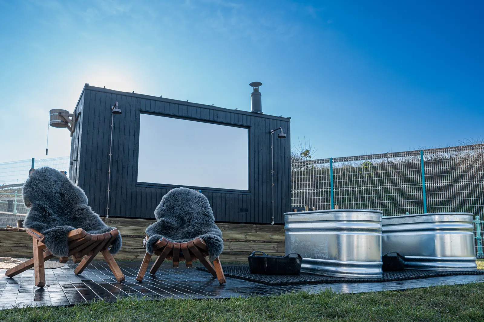 Black timber sauna cabin with sheepskin chairs and two steel plunge tubs on the lido deck