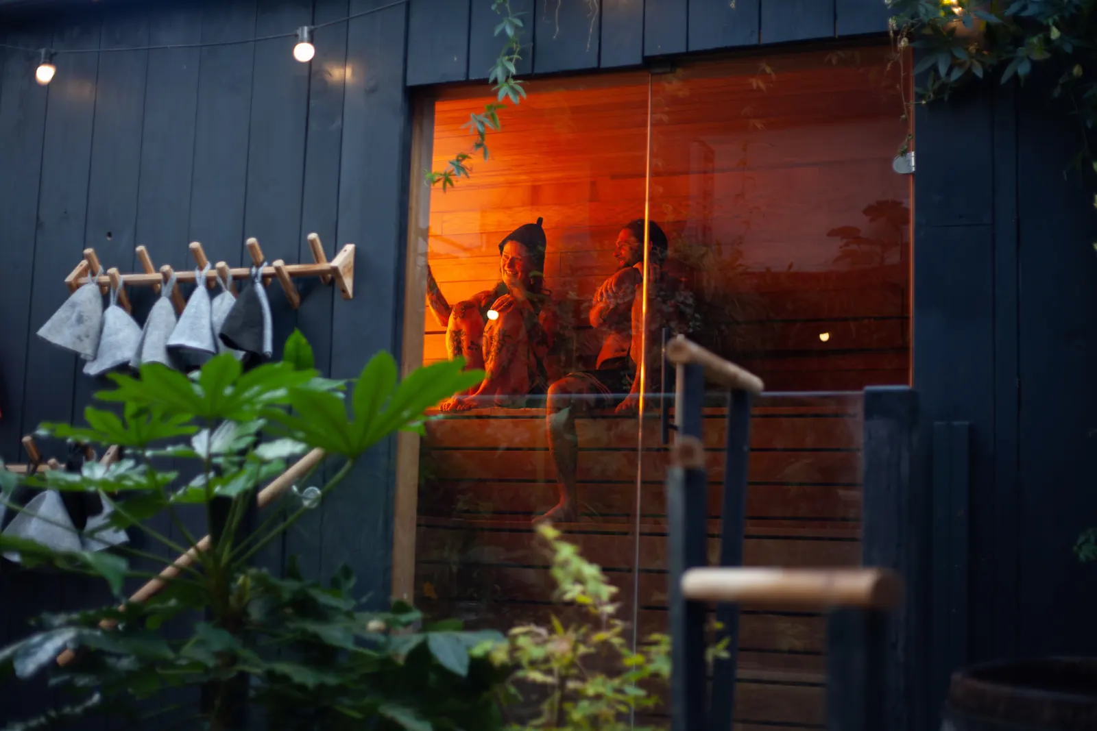 Sauna exterior at dusk with glowing window and hanging hats